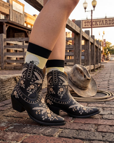 Socksop Cowboy crew socks worn outdoors — rugged frontier-themed pattern paired with boots